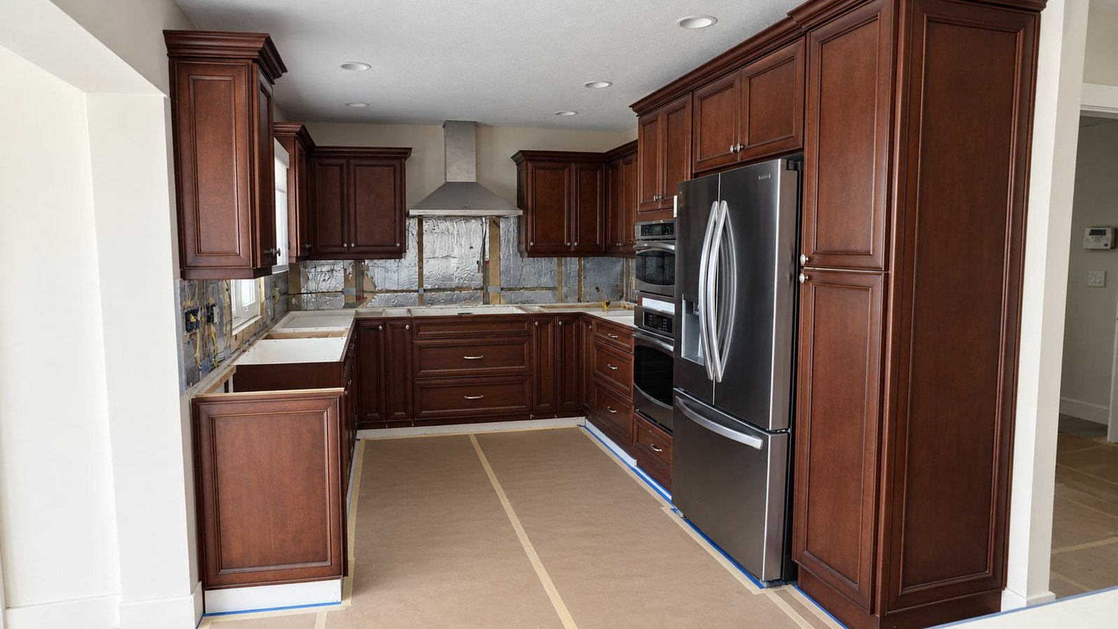 The same kitchen before: dark cherry cabinets and an open, unfinished backsplash wall