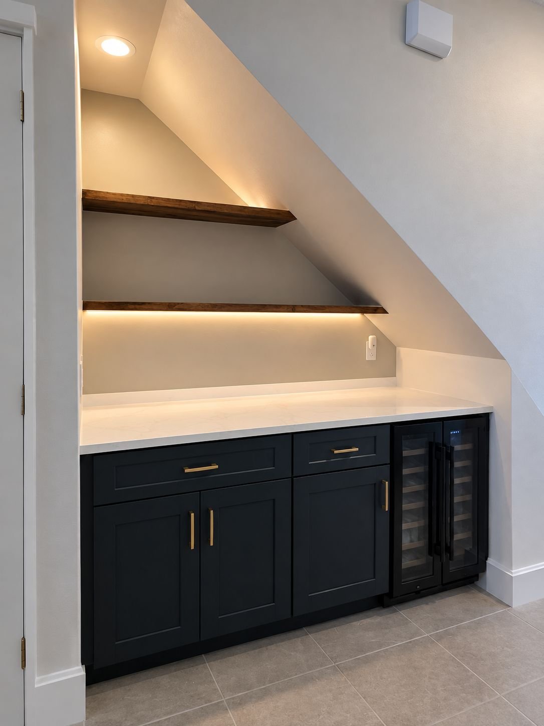 Finished under-stair bar with navy cabinets, white quartz counter, wine cooler and warm-lit wood shelves