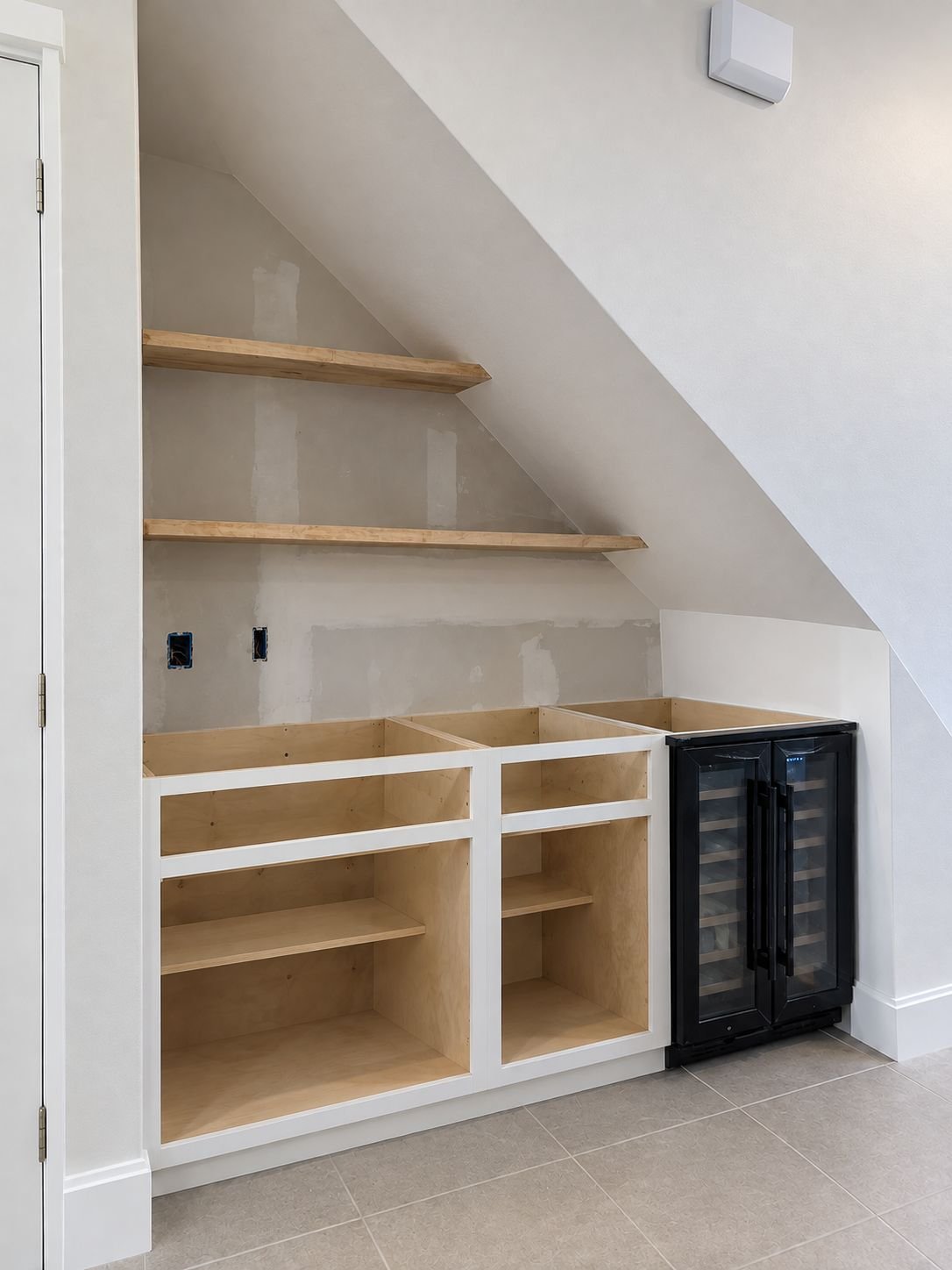 The same under-stair space before: unfinished cabinet boxes, raw shelves and patched drywall